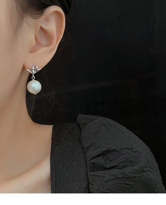 Close-up detail of silver knot pearl earrings on a model with elegant glossy finish