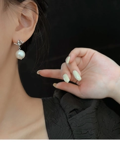 Detail showing elegant knotted silver design with a lustrous white pearl earring on a model