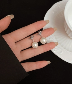 Detail of silver knot stud earrings with large white pearls held by hand against a plate