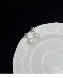 Detailed macro shot of elegant silver knot earrings with white round pearl pendants