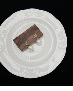 Close-up of pearl drop earrings with silver knot detail on a white ceramic plate
