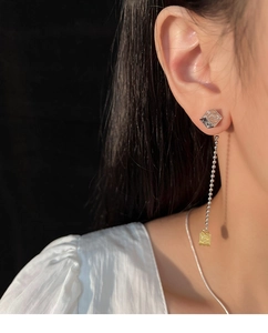 Detail of silver needle earrings with floral cube design and golden tassel chain style