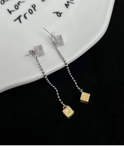 Detail of silver and gold square earrings with long ball chain and wavy texture