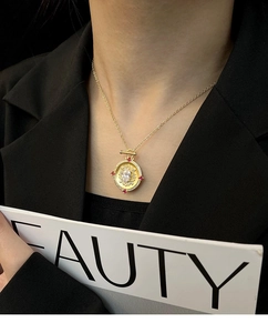 Detailed shot of vintage gold coin pendant with red gemstones on a gold chain necklace