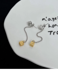 Detail of silver tassel earrings with golden cubes featuring intricate spiral patterns