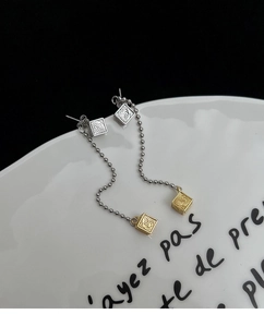 Macro shot of long tassel earrings with silver and gold engraved cubes on chain