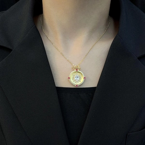 Vintage gold round pendant necklace with clear center stone and red gemstones on black suit