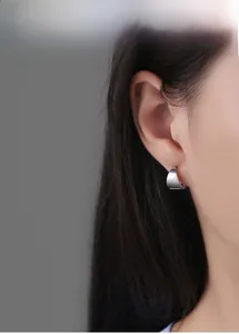 Gros plan d'une boucle d'oreille géométrique argentée minimaliste portée par un modèle