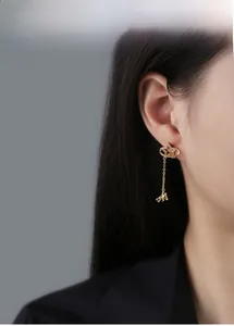 Model wearing gold star stud earrings with a dangling astronaut charm and thin chain