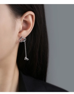 Detail of star-shaped earrings with zircon inlay and hanging bear pendant on ear chain