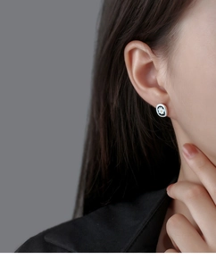 Close-up of minimalist black enamel daisy stud earrings worn on an Asian woman's ear