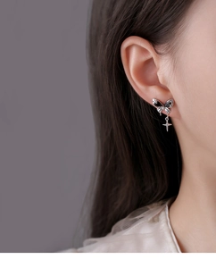 Detail of silver bow earrings with black zircon and a dangling cross star charm