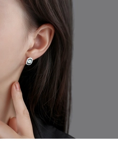 Close-up of a delicate white daisy stud earring with black enamel worn by a model