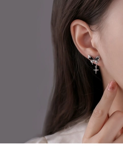 Detail of black bow stud earrings with star pendant and zircon on a model ear