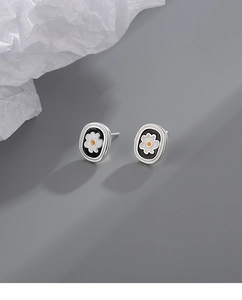 Detail shot of dainty flower stud earrings with black enamel and white petals finish