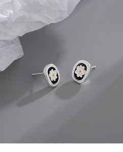 Detail of oval black enamel stud earrings with white daisy floral pattern and S925 finish