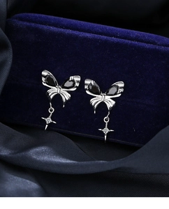 Macro shot of silver butterfly earrings with black gems and a small star pendant charm