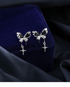 Detail of black bow earrings with zircon butterfly wings and a silver cross pendant