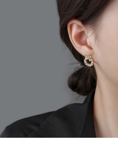Detail of elegant gold bow wreath stud earring with white pearls on model ear