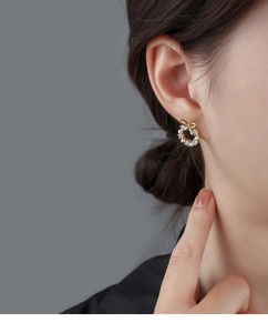 Detailed view of elegant gold bow wreath earrings with pearls and crystals on female model