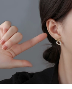 Close-up of golden bow pearl wreath stud earrings worn by a model in detail view