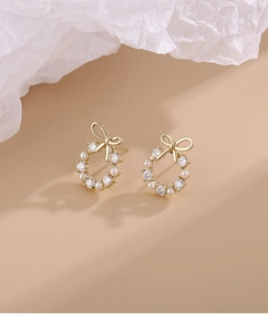 Detailed macro view of gold bow knot pearl wreath earrings with zircon accents