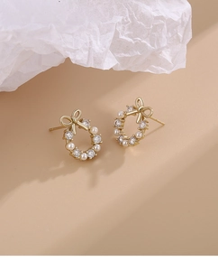 Detailed view of gold bow knot earrings with pearls and zircons on a textured background