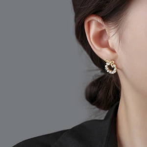 Elegant gold bow earrings with white pearls and crystals worn on model's earlobe
