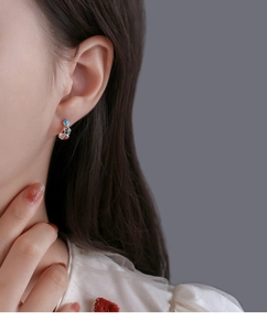 Close-up of silver hoop earrings with colorful enamel floral patterns on a model's ear
