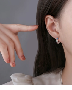 Detailed close-up of a small colorful enamel flower hoop earring worn by a female model