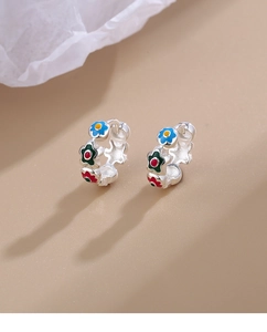 Detail view of silver hoop earrings with colorful enamel flowers on a beige backdrop