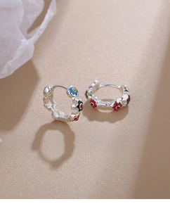 Close-up of silver hoop earrings featuring colorful enamel flowers on a warm beige surface