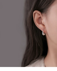 Close-up of minimalist silver water drop earrings worn on ear with polished finish