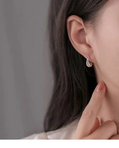 Close-up of minimalist silver water drop earrings worn by a model in a profile view