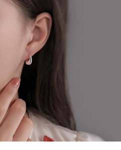 Close-up of woman wearing silver teardrop geometric earrings with a sleek metallic finish