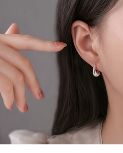 Close-up of minimalist silver water drop earrings worn by a model in a studio
