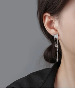 Close-up of asymmetrical silver butterfly earrings with sparkling tassel and gemstone