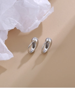 Polished silver teardrop earrings with a sleek mirror finish on a warm neutral background