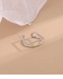 Macro shot of silver minimalist double-layer geometric square ring on warm beige surface