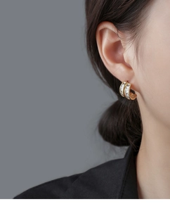 Close-up of gold C-shaped earrings with rectangular zircons worn by a model