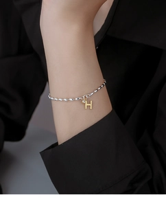 Detail of beaded bracelet with gold H-letter pendant and sparkling zircon on model wrist