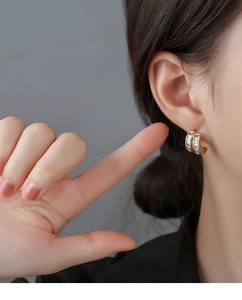 Detail view of gold geometric earrings with rectangular zircons on a model's ear