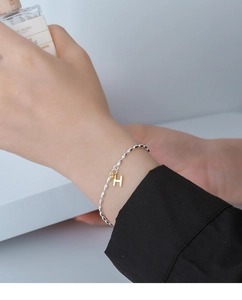 Close-up of a silver bead bracelet with gold H letter pendant and zircon on a wrist