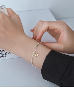 Close-up of beaded silver bracelet with gold H-letter charm and sparkling zircon stones