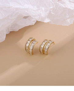 Macro detail of gold C-shape earrings with double row square zircon inlay on textured paper