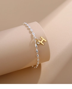 Macro detail of silver oval bead bracelet with golden H letter charm and zircon stone