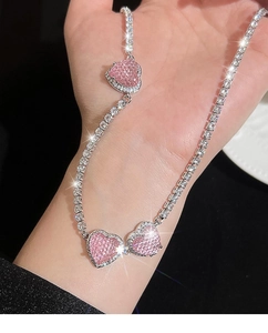 Makro-Detail der silbernen Halskette mit drei rosa Herzanhängern und funkelnder Zirkonkette