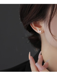 Macro shot of a silver butterfly stud earring with a purple heart-shaped stone on ear