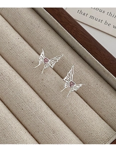Close-up of silver butterfly stud earring with pink heart gemstone in a jewelry box