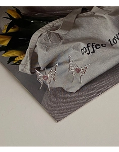 Detailed shot of hollow butterfly earrings featuring pink heart stones on canvas back